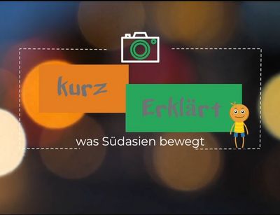 Das Bild zeigt ein visuelles Konzept für ein Projekt mit dem Titel "kurz Erklärt" und dem Untertitel "was Südasien bewegt". Das Design enthält zwei farbige Rechtecke: ein orangefarbenes mit dem Text "kurz" und ein grünes mit dem Text "Erklärt". Oben auf dem Bild ist ein Icon einer Kamera abgebildet. Rechts vom Text befindet sich eine kleine Figur mit einem gelben Hemd und blauer Hose. Der Hintergrund des Bildes ist verschwommen und zeigt Bokeh-Lichteffekte. In der unteren rechten Ecke steht der Hinweis "Made with VISME".