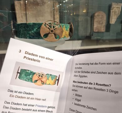 Diadem aus Kupfer im Hintergrund, davor aufgeschlagenes Heft mit Text.