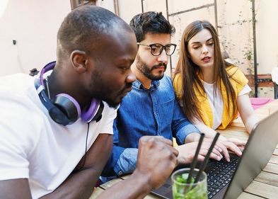 Drei junge Menschen sitzen am Computer und besprechen sich